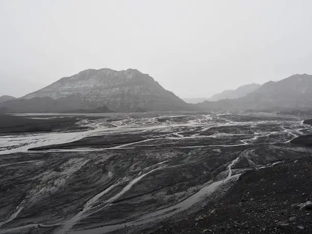 Dark and rainy day on a glacier in Iceland, with streams of water pouring down  from the glacial icecap, which is entirely covered with volcanic ash. 

The whole scenery is very surreal, as there is essentially no colours except all shades of grey...