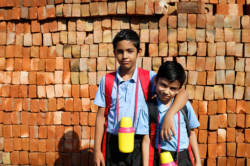 Elementary student of Indian ethnicity portrait with school bag and water bottle on brick background