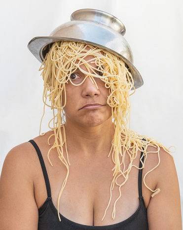 woman with a strainer of spaghetti on her head as a hat and spaguetti as hair wig. mental issues concept.