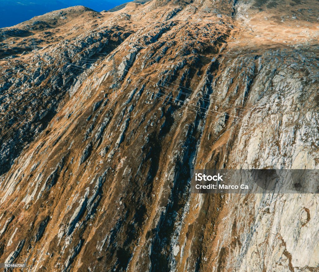 aerial view of the striking rock surface of a swiss mountain landscape view of a sloping rock face with grooves and furrows. a power pole and power line runs along the mountain. Near the famous swiss mountain pass roads Grimselpass and Furkapass Mountain Road Stock Photo