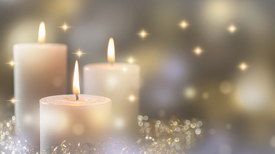 three white burning candles on bright blurred background with copy space, glittering lights and sparks in festive atmosphere, greeting card for christmas, happy new year or other holidays