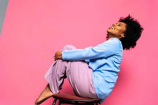 Happy young woman sitting on a bench on a pink background