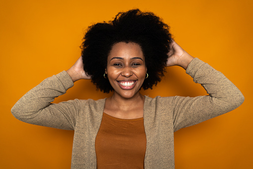 Portrait of a young woman touching hair on orange background