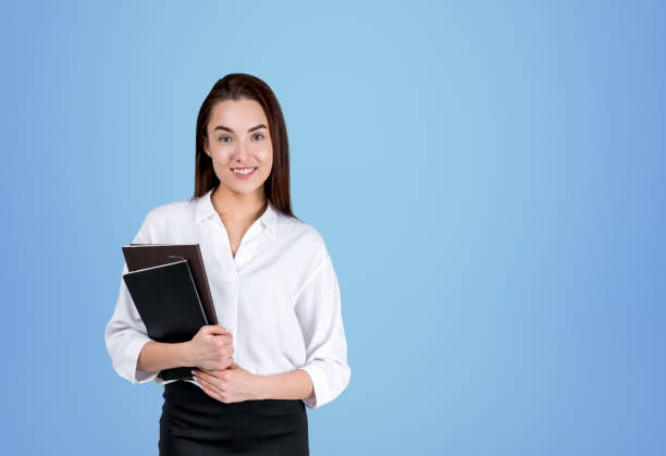 istock Young businesswoman with notebook, smiling on blue background 1424871919