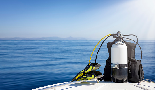 A scuba diving tank and gear standing on a boat bow with blue sea and sunshine as a banner with copy space