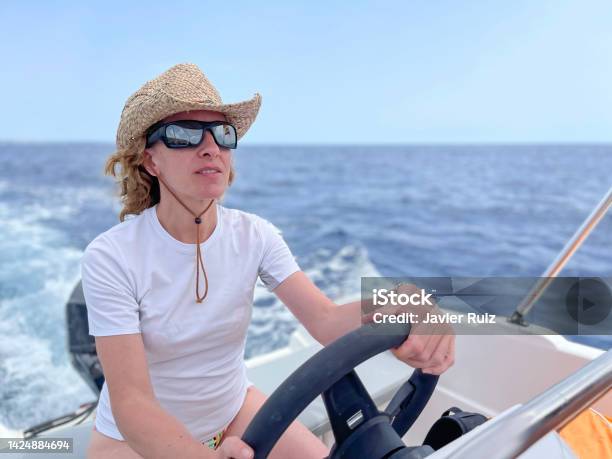 A Smiling Woman With Sunglasses And Straw Hat Driving A Sports Boat On A Blue Water Sea On A Summer Vacation Day Selective Focus Copy Space Stock Photo - Download Image Now