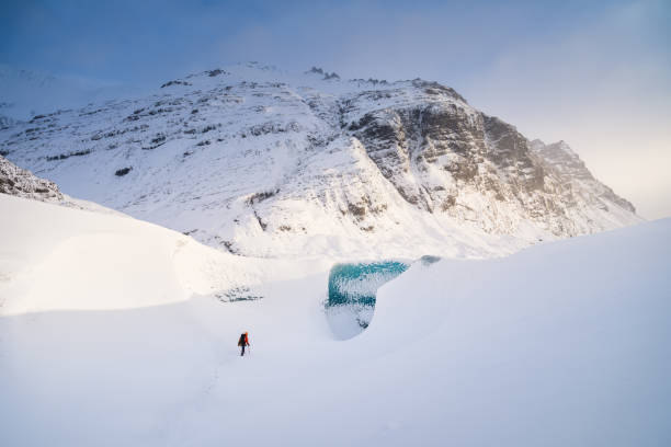 アイスランドの氷の洞窟の入り口の前にいる男。氷河の上を歩く。夜明けの高い山と雲。ヴァトナヨクル国立公園でアイスランドを旅する。 - ice cold glacier blue ストックフォトと画像