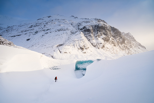 A man in front of the entrance to an ice cave in Iceland. A walk on the glacier. High mountains and clouds at dawn. Travelling through Iceland in a Vatnajokull National Park.