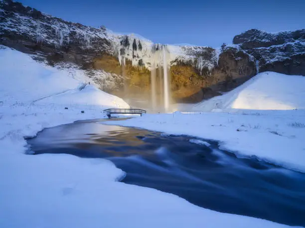 Photo of Seljalandsfoss waterfall, Iceland. Icelandic winter landscape.  High waterfall and rocks. Snow and ice. Powerful stream of water from the cliff. A popular place to travel in Iceland.