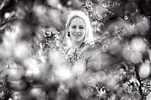 black and white portrait of a smiling blonde woman in a blossoming spring garden, selective focus