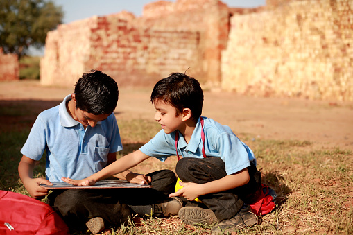 Elementary students of Indian ethnicity sitting together outdoor and studying portrait close up during summer season.