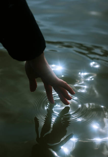 A mystique picture of a hand gently touching water with bright reflections of sunlight