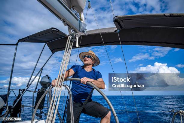 A Man Wearing A Straw Hat Is Driving A Sailboat And Enjoying It Stock Photo - Download Image Now