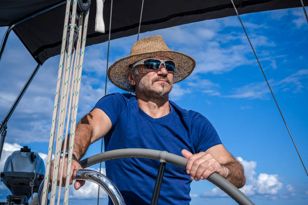 a man wearing a straw hat  is driving a sailboat and enjoying it. - yacht nautical vessel autopilot sailing imagens e fotografias de stock