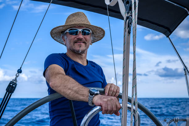 a man wearing a straw hat  is driving a sailboat and enjoying it. - yacht nautical vessel autopilot sailing imagens e fotografias de stock