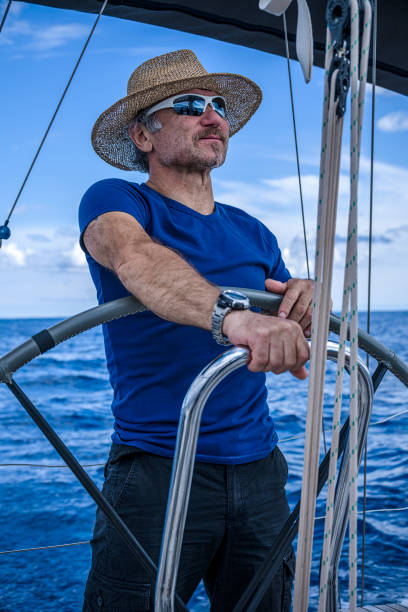 a man wearing a straw hat  is driving a sailboat and enjoying it. - yacht nautical vessel autopilot sailing imagens e fotografias de stock