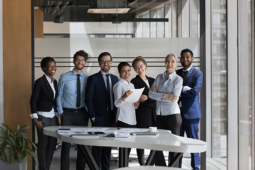 Gorgeous smiling businesswoman in suit standing in office with hands crossed. In background her successful team posing.