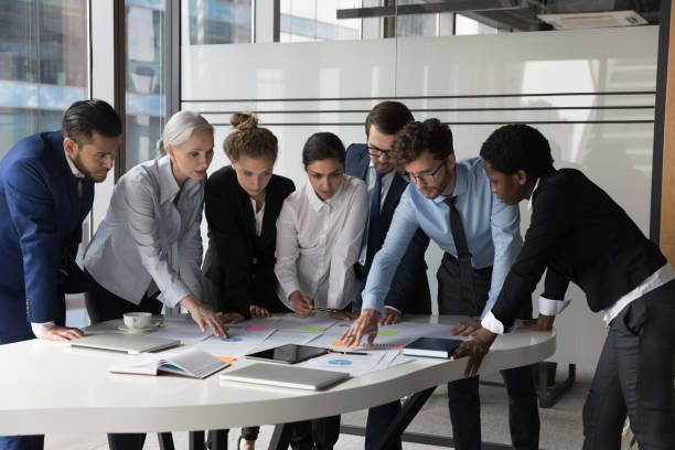 Diverse different aged business group standing at meeting table Diverse different aged business group standing at meeting table, negotiating on marketing reports, statistic diagrams, working on startup project together, using scrum approach with sticky notes scrum stock pictures, royalty-free photos & images