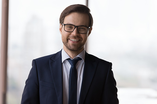 Happy successful business leader in glasses and formal suit head shot portrait. Confident millennial businessman, CEO, company owner, director looking at camera, smiling, laughing