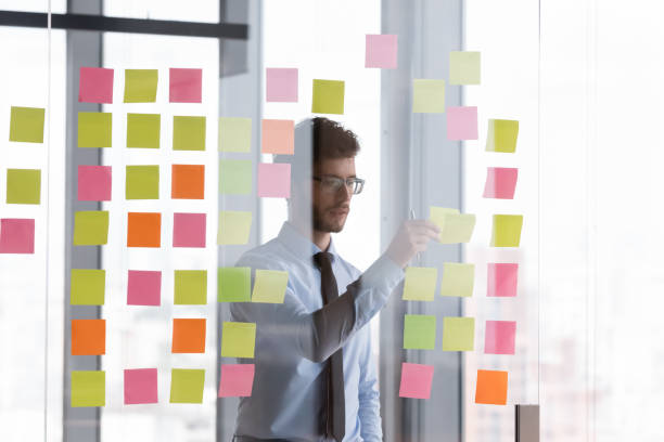 istock Focused millennial businessman sticking paper notes on glass wall 1424912721