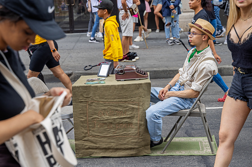 6th Avenue, Manhattan, New York, NY, USA - July 16th 2022: Young male author waiting for inspiration or customers at a street market