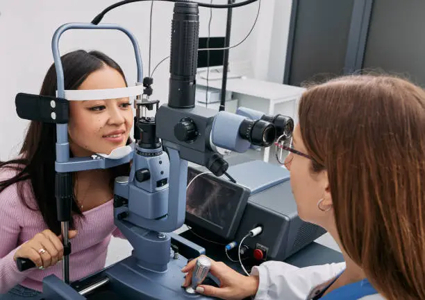 Korean woman while eye exam with binocular slit-lamp at ophthalmology clinic with experienced female optometrist