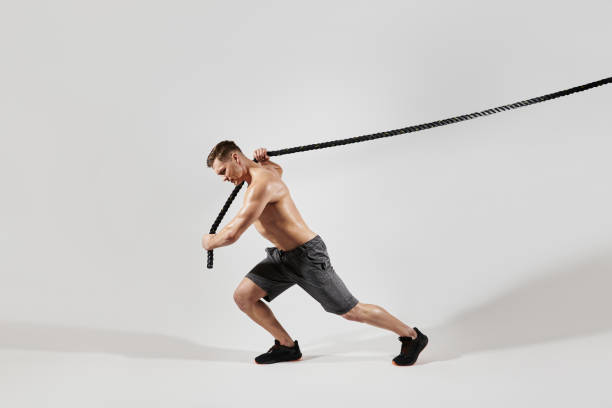 Confident young man with perfect body pulling a rope against white background stock photo
