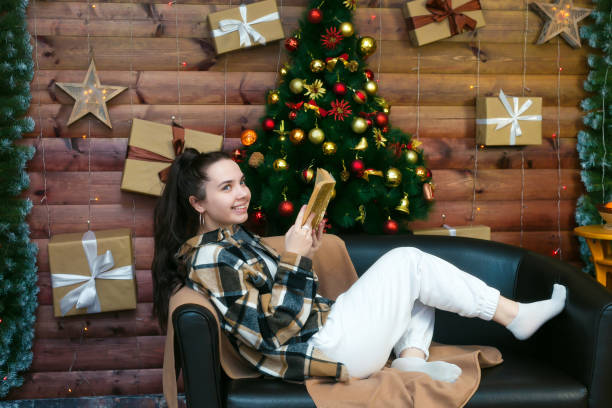 une jeune fille au sourire espiègle lit un livre allongé sur le canapé le soir du nouvel an - new year wall decoration gift photos et images de collection