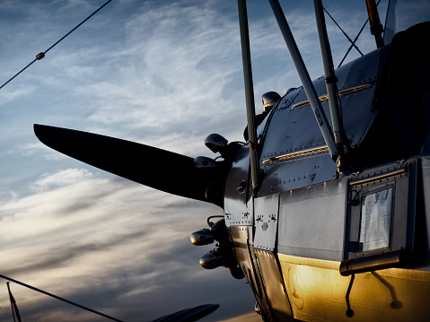 An old aeroplane/airplane. A biplane’s propeller against the sky. The setting sun is reflected in the aircraft’s golden yellow undercarriage.