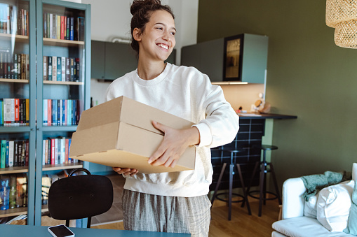 A young woman holding a cardboard boxes with online orders in the living room