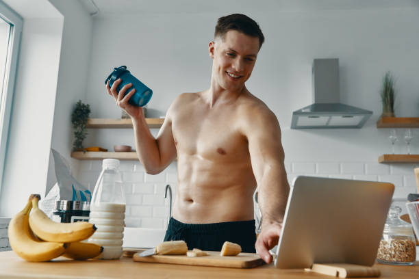 istock Happy young man preparing protein drink and using digital tablet while standing at the kitchen 1424928473