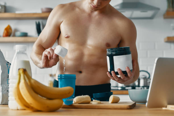 istock Handsome fit man preparing protein drink while standing at the kitchen 1424929760