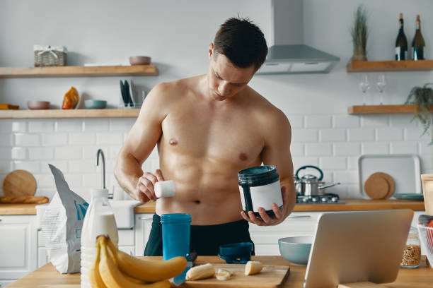 istock Handsome fit man preparing protein drink while standing at the kitchen 1424929845