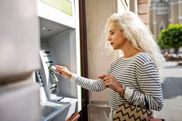 Mature woman using an ATM holding shopping bags stock photo