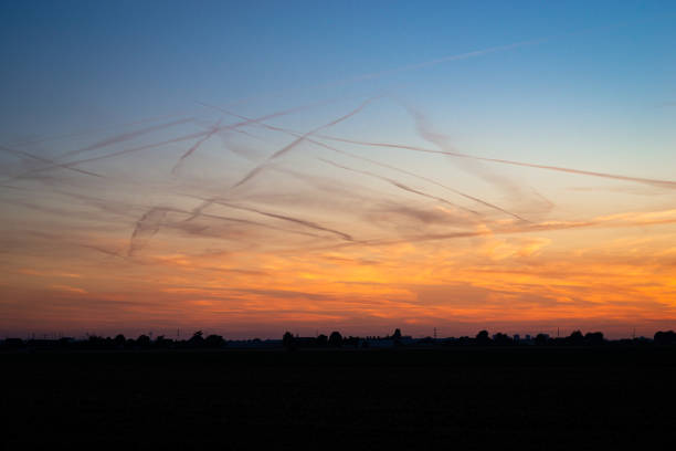 Many water vapor trails from aircraft, also called contrails, contrast with the colorful twilight sky.