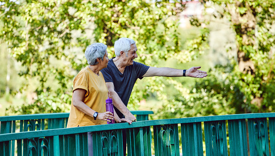 Attractive middle-aged old couple, wife and husband enjoy a walk and communication in summer park during morning sportive stroll with water. Communication, carefree healthy retirement