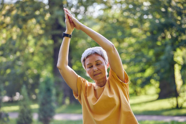 istock Older Asian woman makes stretching exercises in summer park 1424946283