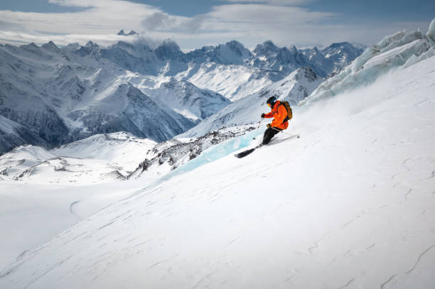 A skier in bright sports equipment goes down the glacier against the backdrop of a cloudy sky and snow-capped mountains stock photo