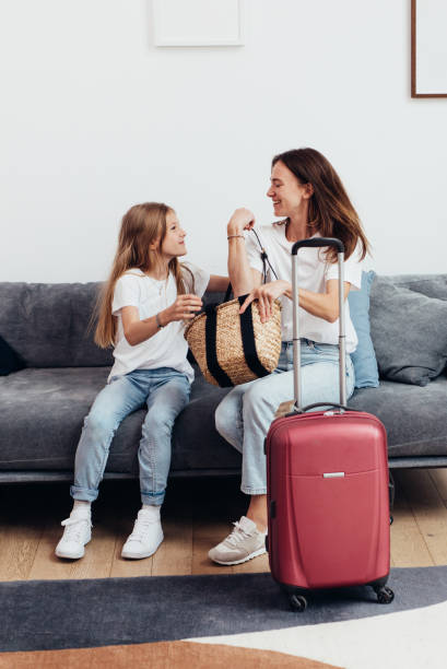 istock Mother and daughter sitting on the couch with a suitcase 1424954476