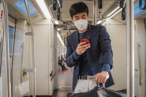 istock Asian businessman passenger man in suit wearing protective face mask using mobile phone and standing inside BTS sky train or MRT underground train at railway platform while traveling to work 1424957013