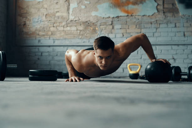 Confident young man using medicine ball while doing push-up exercises in gym stock photo