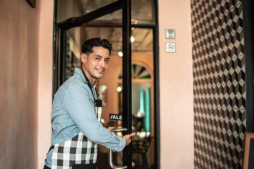 Portrait of mid adult waiter / owner opening up the entrance door
