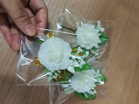 Hand Holding Pretty White Artificial Flowers with Green Leaves. The Most Popular Mother's Day Flowers in Thailand.