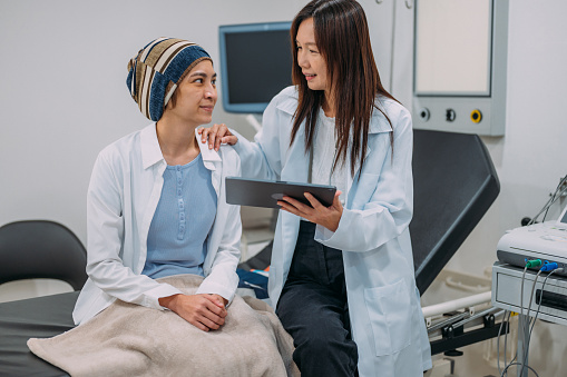 An Asian female gynecologist talking to her patient about cervical cancer awareness and test results on an electronic wireless tablet.