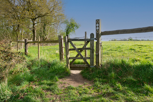 Public footpath leading through gate and across fields in the English countryside, with signs indicating direction to be followed for ramblers to follow.