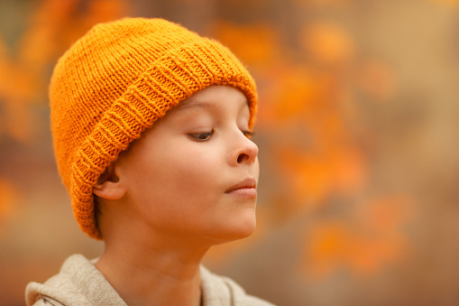 Boy in a hat is smiling in the autumn park. Bright colour background. Close up portrait of a cheerful boy.Funny portrait when kid is looking at his nose