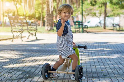 2 year old blond toddler playing and enjoying a sunny day in the park with his tricycle.