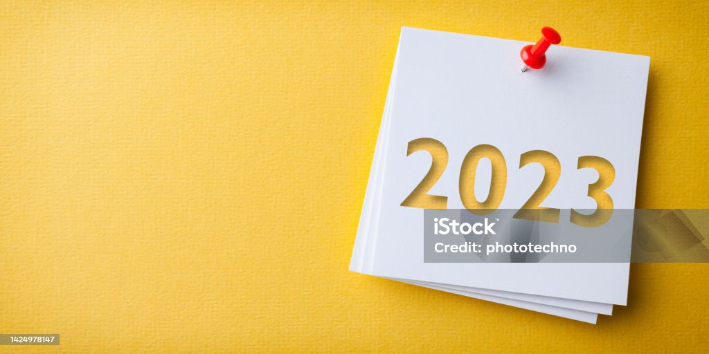 White Sticky Note With Happy New Year 2023 And Red Push Pin On Yellow Cardboard Background 2023 Stock Photo