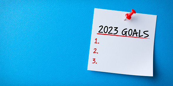 White Sticky Note With New Year 2023 Resolutions And Red Push Pin On Blue Chardboard