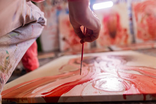 Motivated artist, using paint and paintbrush while working on a new piece of art from his messy home studio/workshop